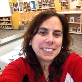 headshot of Nicole in red shirt with library in background